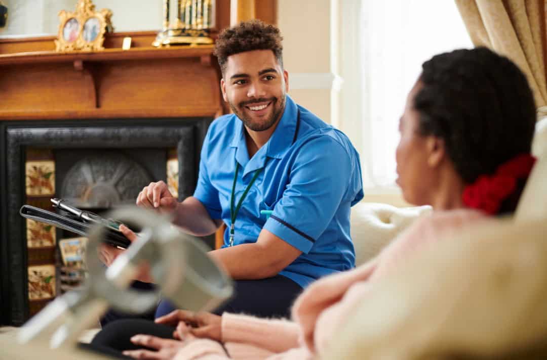 Male care workers smiling and having a friendly conversation with his service users in a bright living room setting.